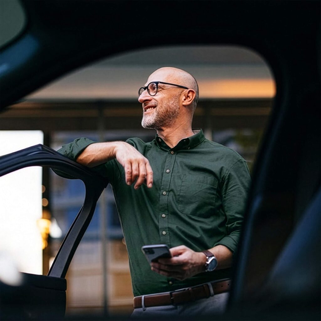 Someone is holding a mobile phone by a car, looking out.